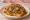 Kentucky Burgoo Sandwich: an illustration of beef, pork, onion, tomato and more on burger bun.