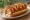 Korean Corn Dog — Sandwich Version: an illustration of sausage, mozzarella, ketchup and mustard on hot dog bun.