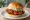 Kyochon Chicken Sandwich: an illustration of chicken, maggi seasoning sauce, garlic, honey and more on burger bun.