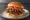 Lotteria — Bulgogi Deluxe: an illustration of beef, bacon, tomato and bbq sauce on burger bun.