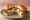 Lotteria — Mozzarella Bacon Burger: an illustration of beef, bacon and mozzarella on burger bun.