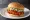 Lotteria — Spicy Chicken Burger: an illustration of chicken and hot sauce on burger bun.