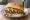 Maid-Rite: an illustration of beef, onion, pickle and mustard on burger bun.