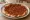 Manoushe Muhammara (منقوشة محمرة): an illustration of pepper, walnuts, brown sauce, olive oil and more.