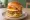 Mom's Touch — Unbelievable Burger: an illustration of chicken, shrimp, egg, sriracha and more on burger bun.