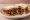 Oakland Soul Food Sandwich: an illustration of chicken, pork, hot sauce and pickle on white bread.