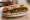 Panuozzo con Salsiccia e Friarielli: an illustration of sausage, pork, garlic, olive oil and more on ciabatta.