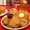 Fried chicken and a butter-topped waffle with syrup on a red table, cornbread muffins and iced tea in a jar behind.
