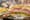 A deli sandwich cut in half on a metal cake stand, layered meats, cheese, tomato and lettuce, frittata slices beside it.