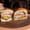 A turkey, cheddar and avocado sandwich on a Dutch crunch roll, cut in half on a round wooden board, dining chairs behind.