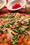 Close-up of a pizza topped with mushrooms, artichoke and basil on a red tablecloth, bowls and a cheese shaker behind.
