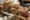Wire baskets piled with fresh bagels stacked on a rolling steel table in a bakery kitchen, ovens behind.