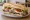 Sándwich de Bodegón: an illustration of beef, pork, cheese, lettuce and more on baguette.