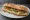 Sandwich Houmous: an illustration of hummus, cucumber, tomato, olive oil and more on baguette.