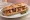Sandwich Rillauds d'Anjou: an illustration of pork belly, mustard, pickle and pepper on baguette.