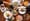 Overhead view of a wooden table crowded with plated dishes and a charcuterie board as four hands clink wine glasses.