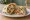 Shawarma de Pollo: an illustration of chicken, tahini, tomato, onion and more on pita.