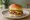 Slider: an illustration of beef, onion, pickle and american cheese on burger bun.