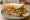 Soft Shell Crab Sandwich: an illustration of tartar sauce, lettuce, tomato and lemon on white bread.
