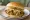 South Carolina BBQ Sandwich: an illustration of pork, mustard, coleslaw and pickle on burger bun.