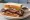 Texas BBQ Brisket Sandwich: an illustration of beef, pickle, onion and bbq sauce on white bread.