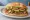 Torta de Carnitas: an illustration of pork, refried beans, avocado, lettuce and more on bread.