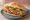 Torta de Milanesa de Cerdo: an illustration of pork, egg, refried beans, avocado and more on bread.