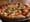 A margherita pizza with sliced tomato, melted mozzarella and torn basil on a metal pan on a wooden table.